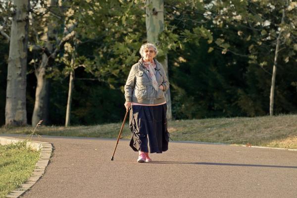 Older woman walking in a park with the help of a cane.